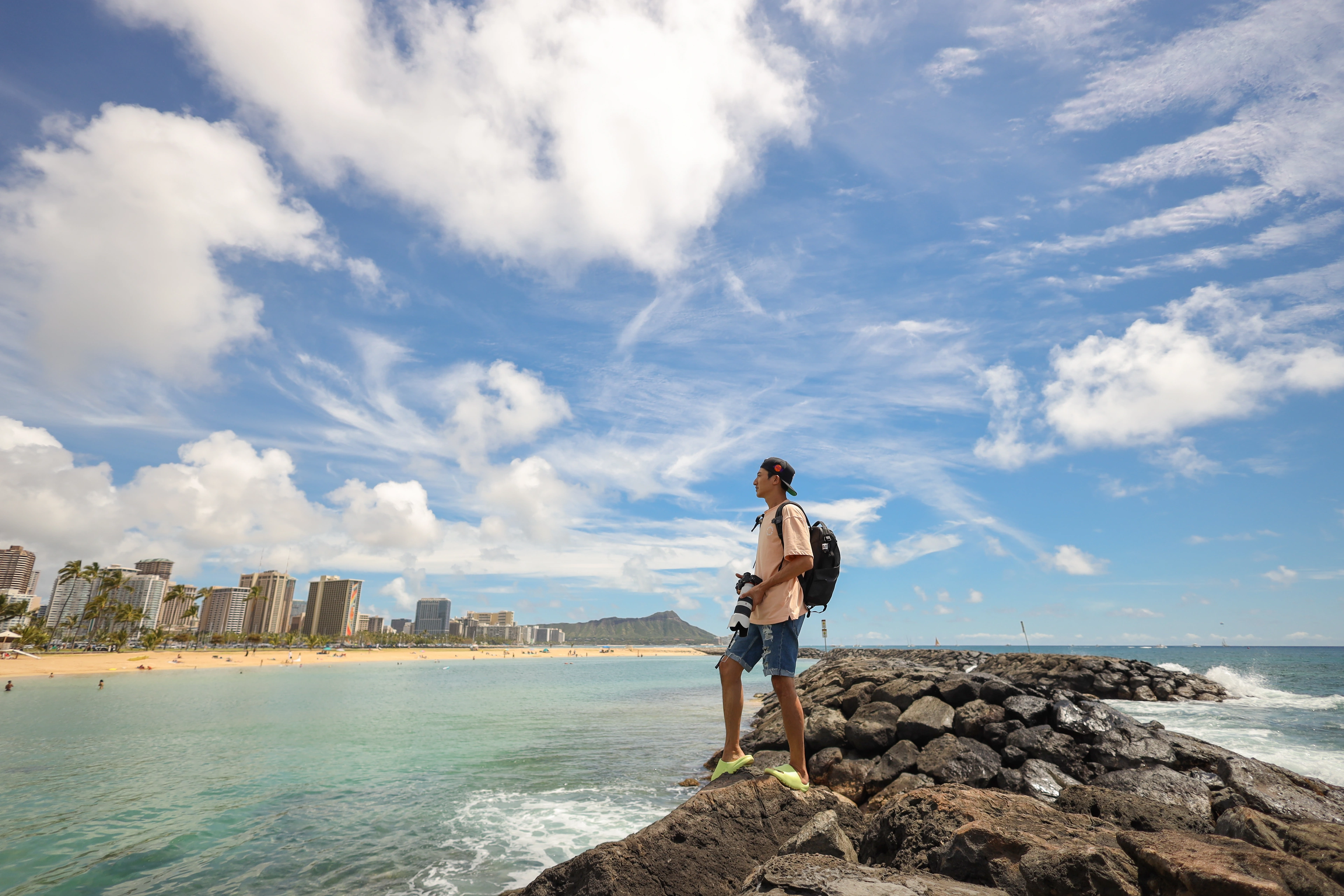 David carrying a camera on the rocks beside Waikiki