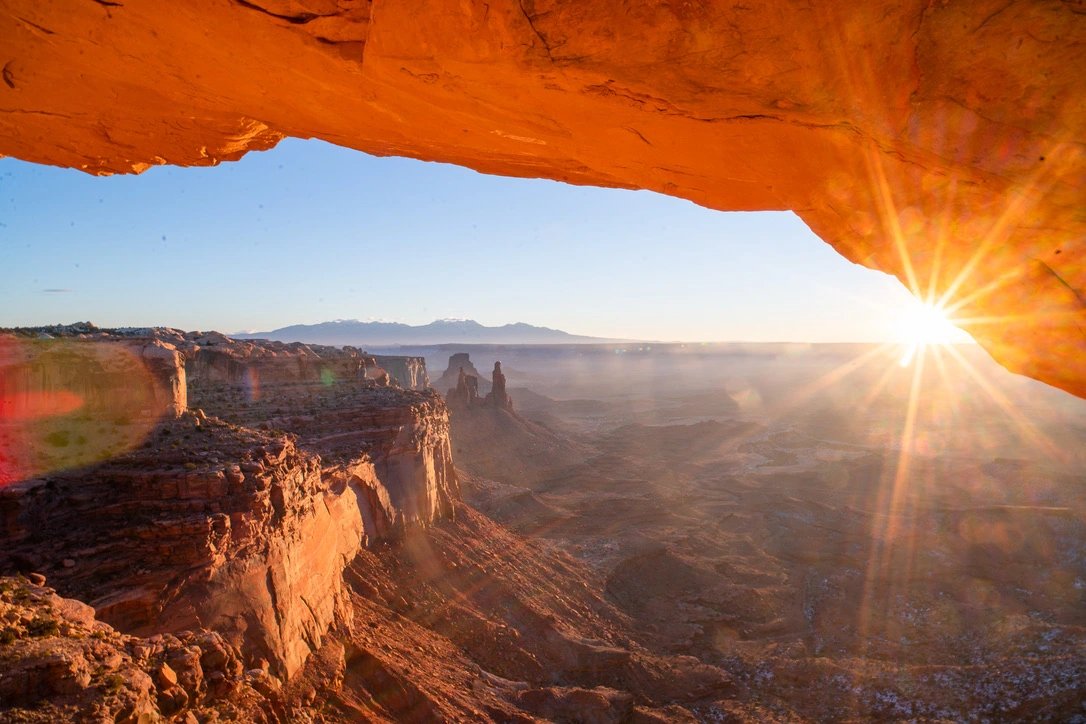 Sunrise shining through a stone arch above a vast canyon