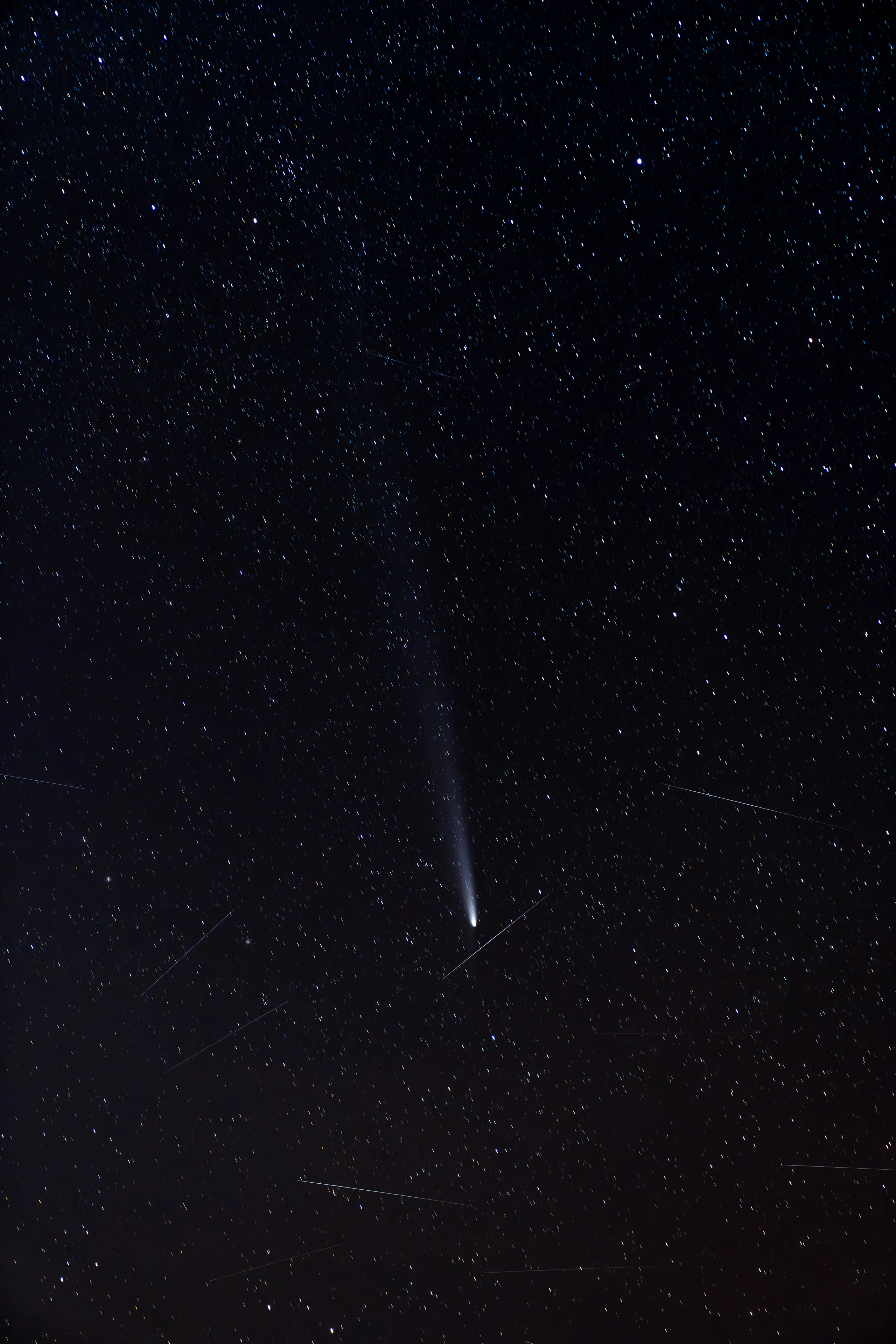 A comet surrounded by stars and faint satellite trails