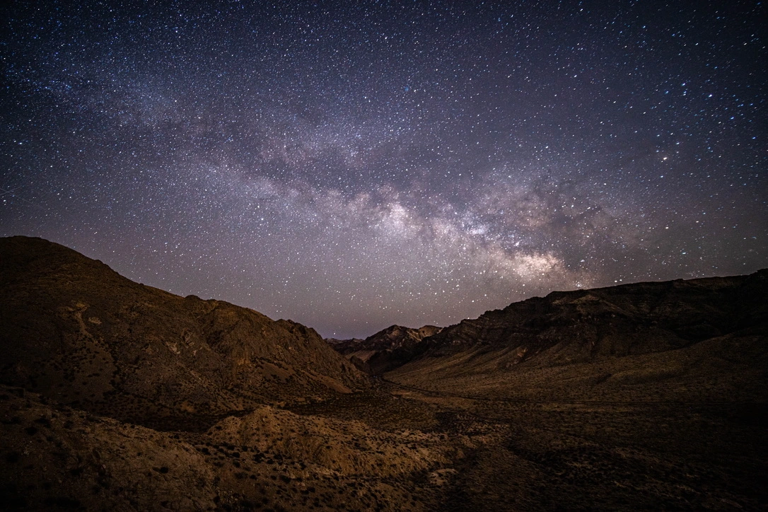 The Milky Way above a dark desert valley between ridges