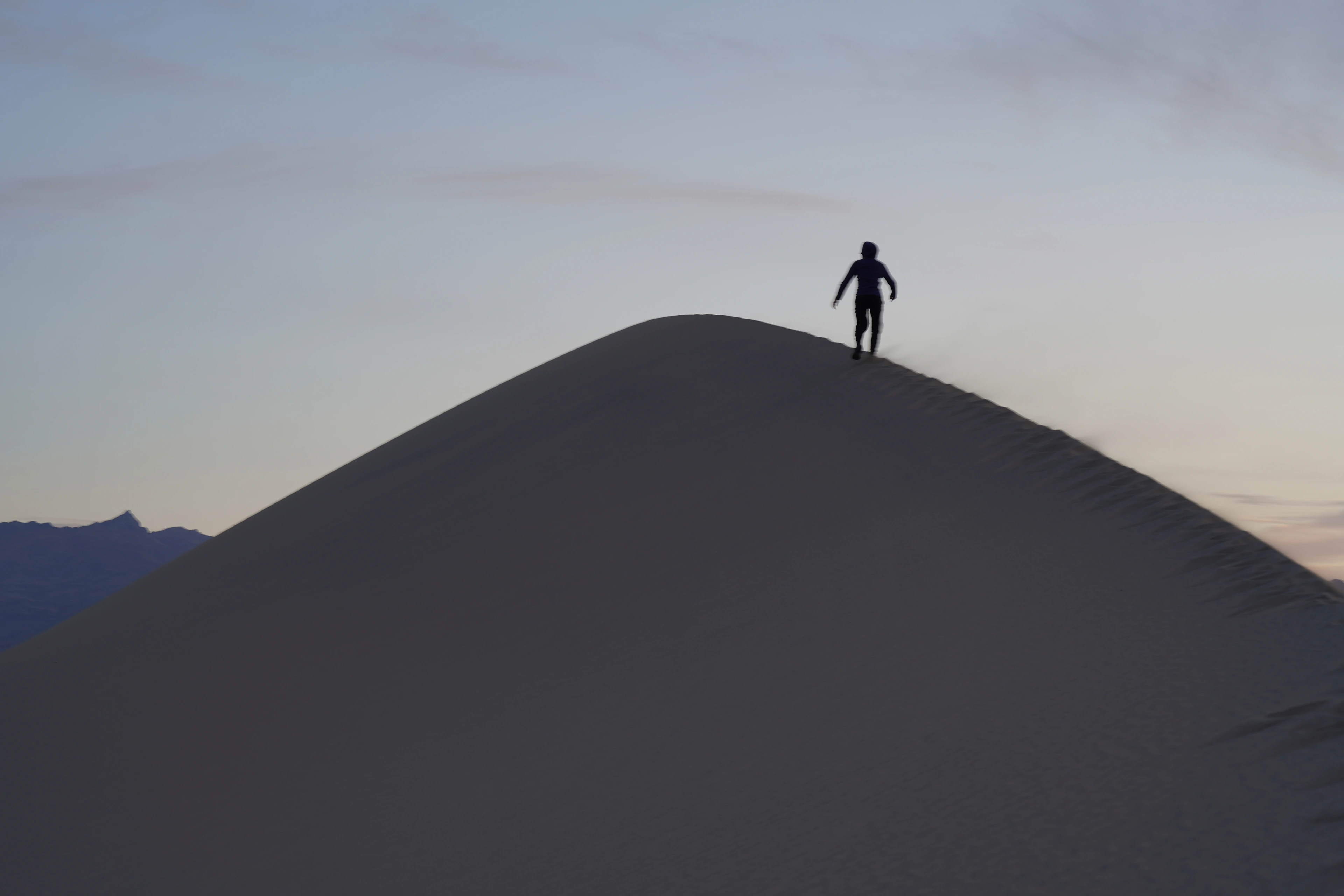 A solitary figure standing on the crest of a dark sand dune