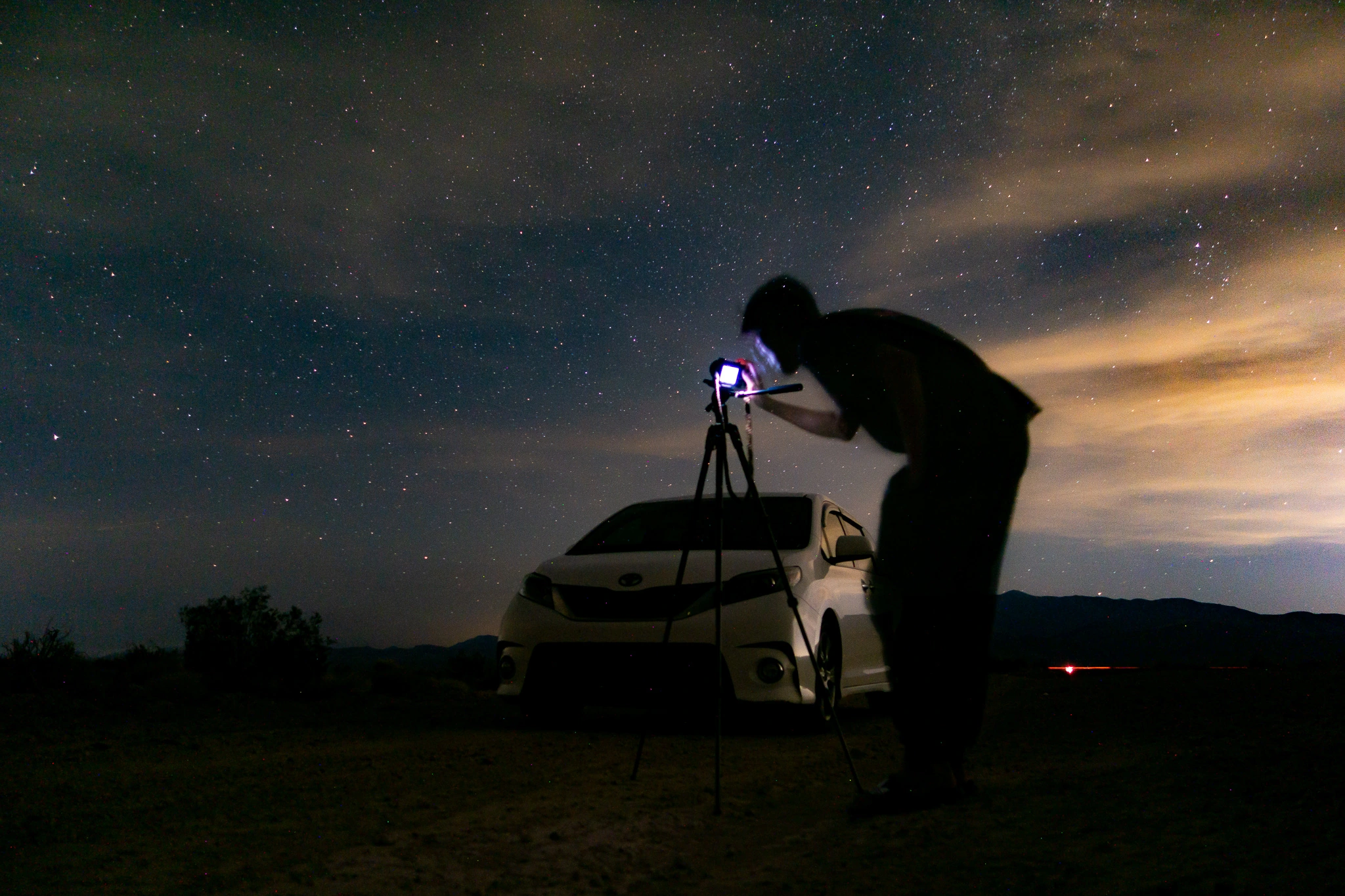 A photographer working beside a car beneath a clouded night sky