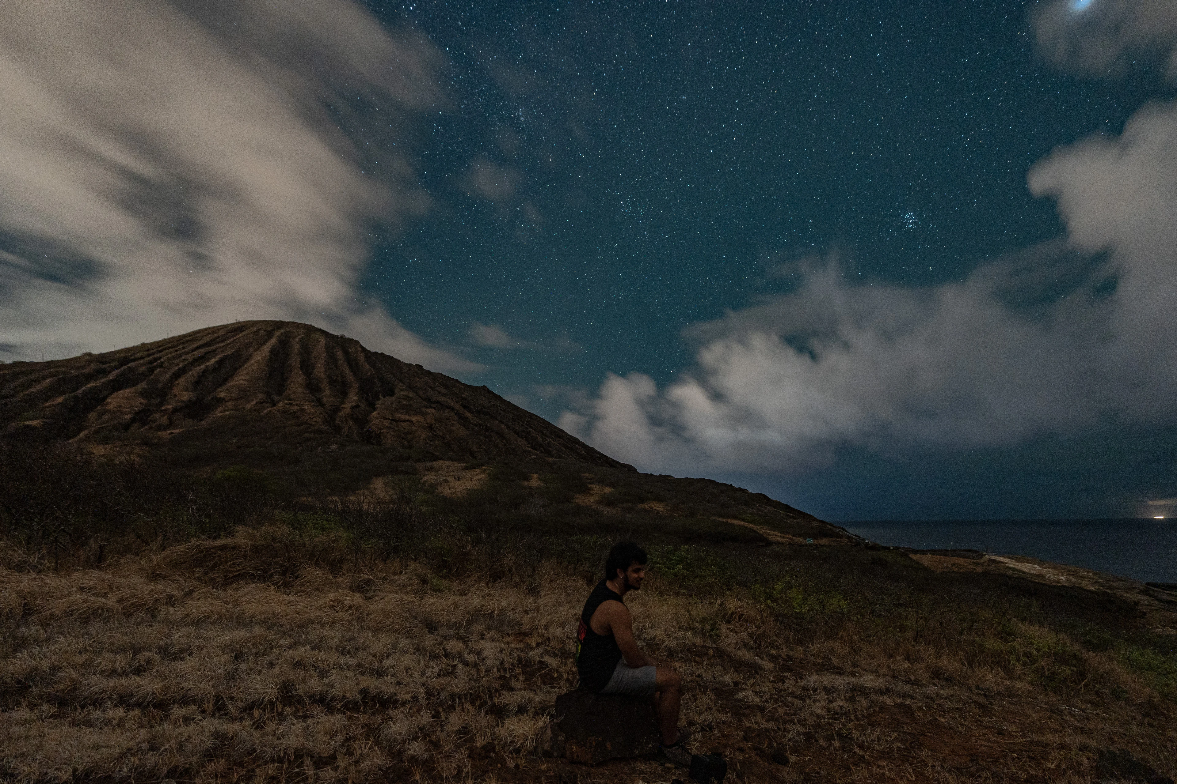 A seated figure beneath stars and clouds beside an East Oahu crater