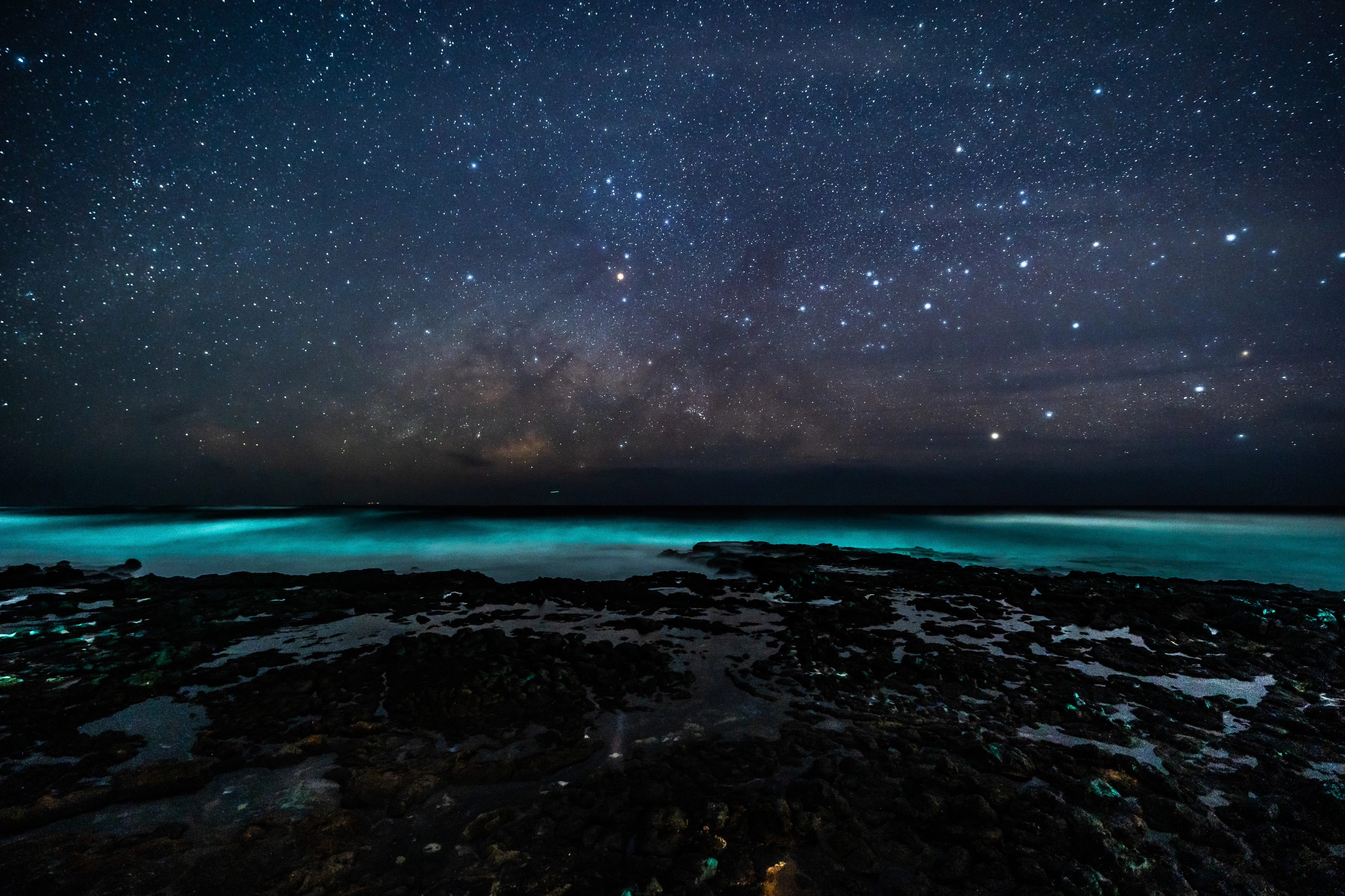 A turquoise night sea beneath a sky filled with stars at Kaloko Beach