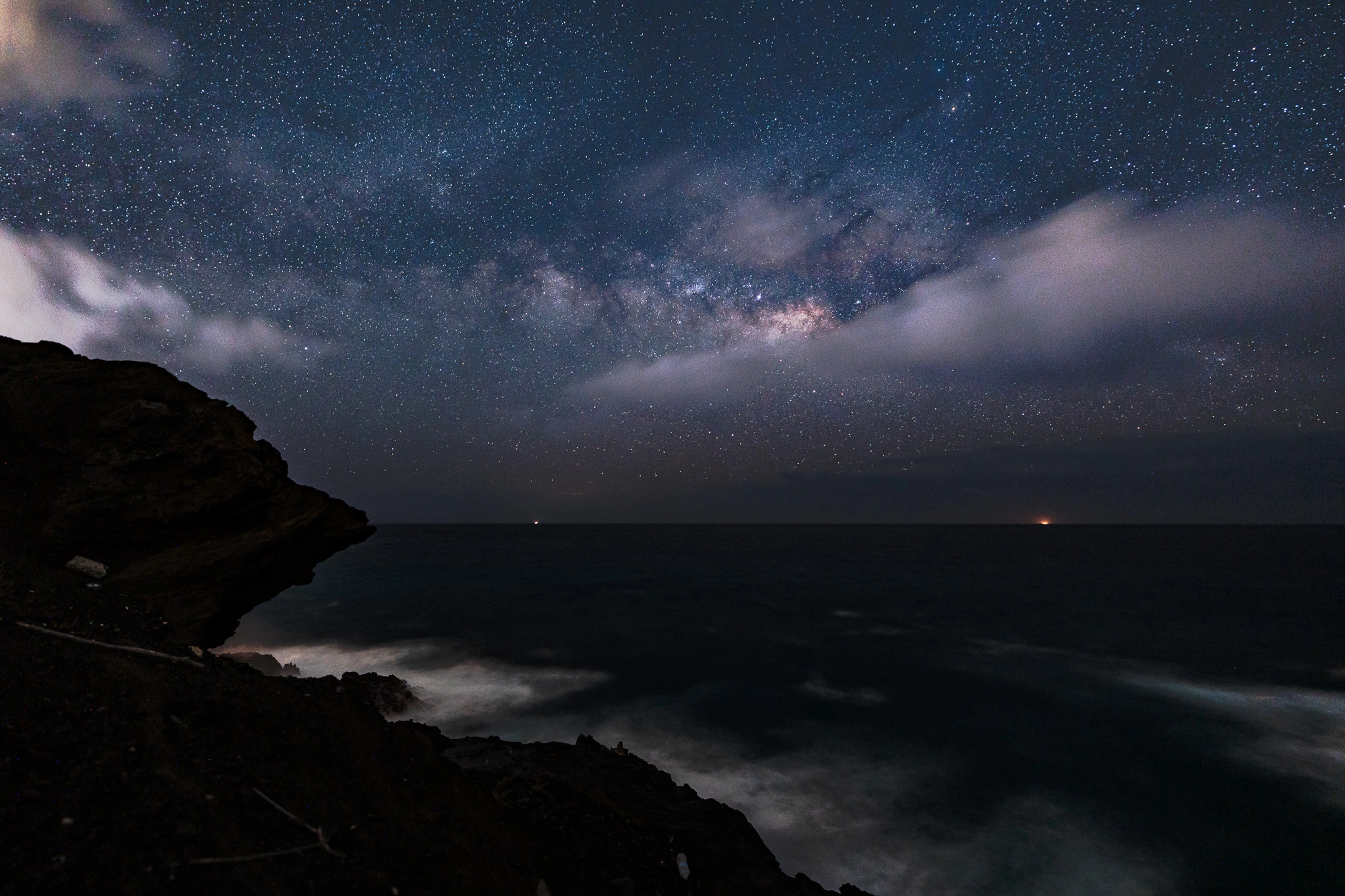 The Milky Way and clouds above the dark coast of East Oahu