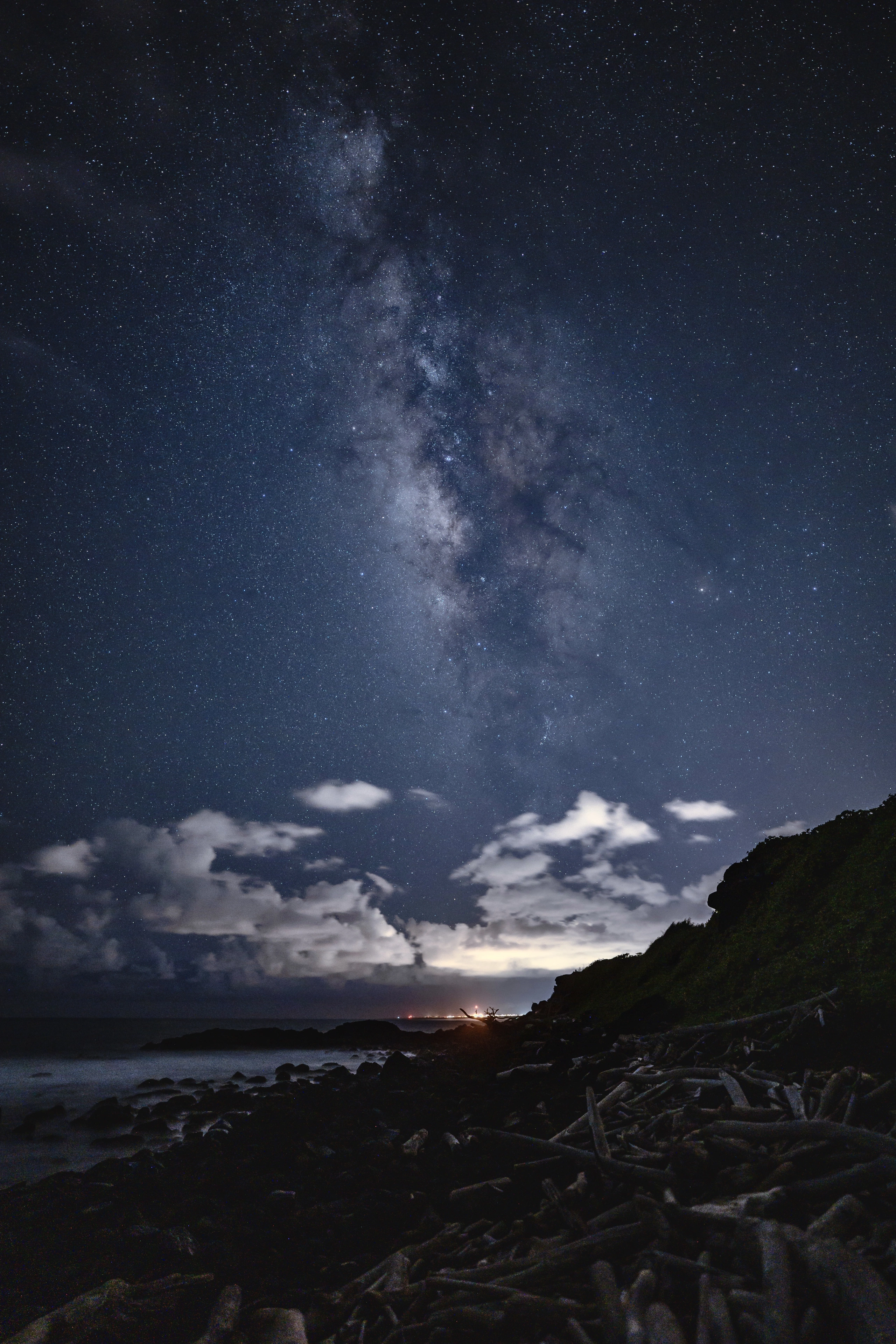 The Milky Way above clouds, driftwood, and the dark Kapaʻa coast