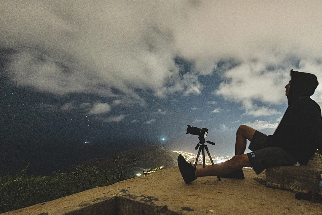 A photographer resting beside a tripod above city lights