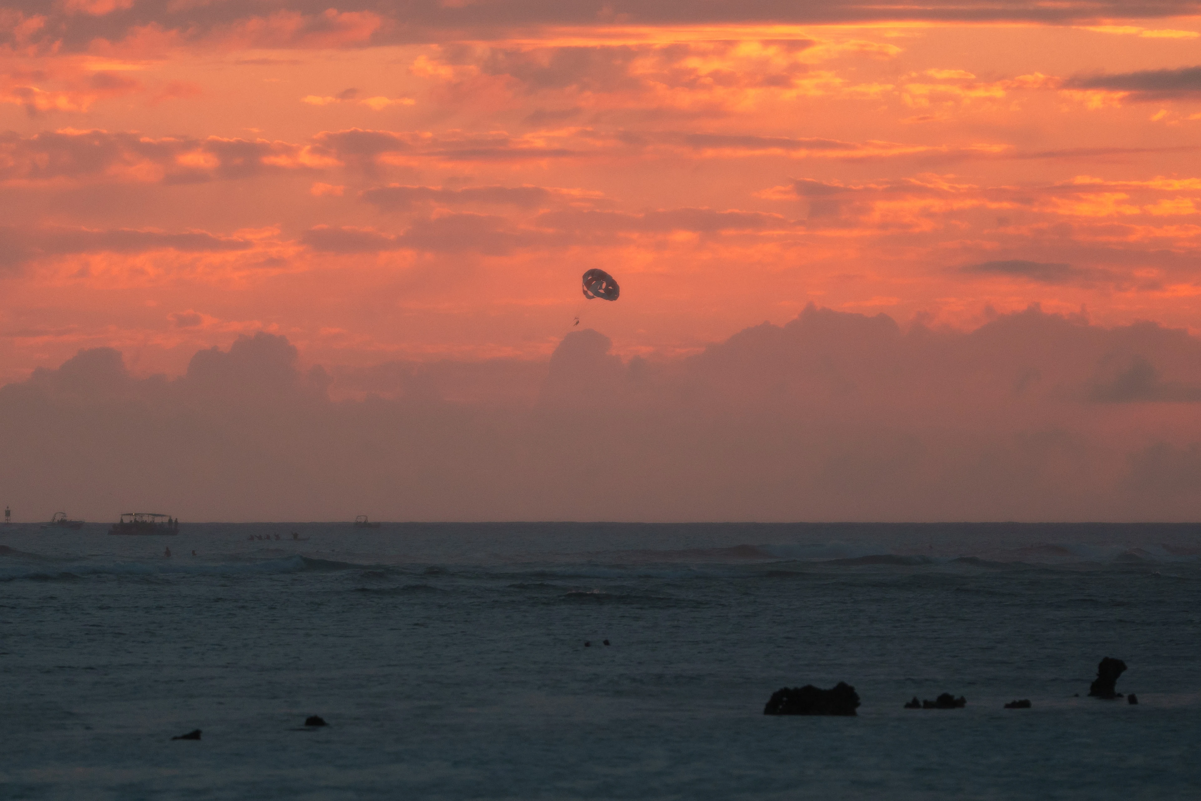 A parasail silhouetted against an orange sunset above the Pacific