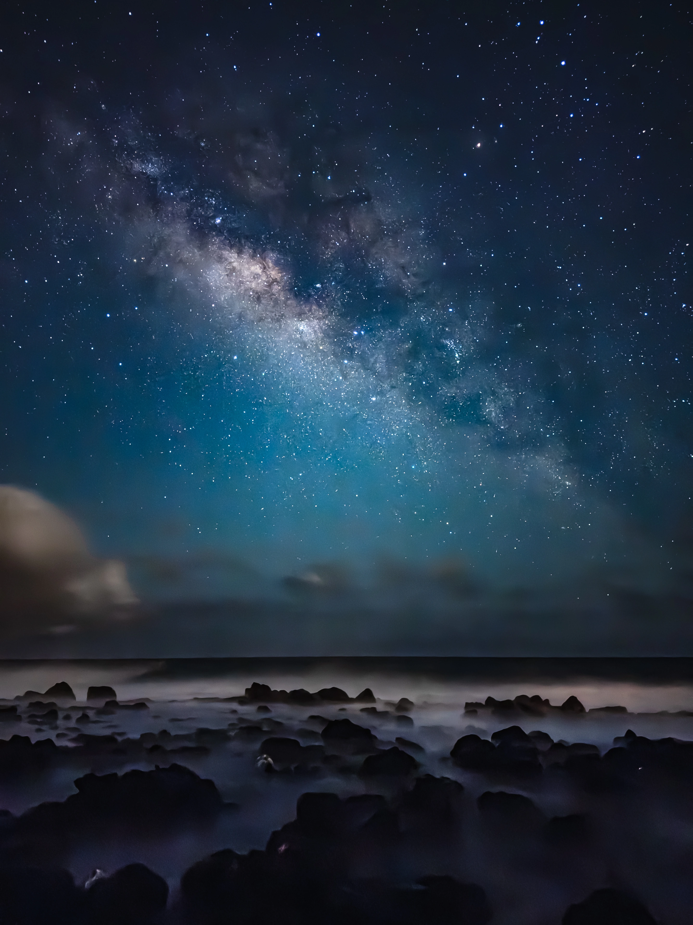 The Milky Way above dark rocks and white surf at Poipu, photographed with an iPhone