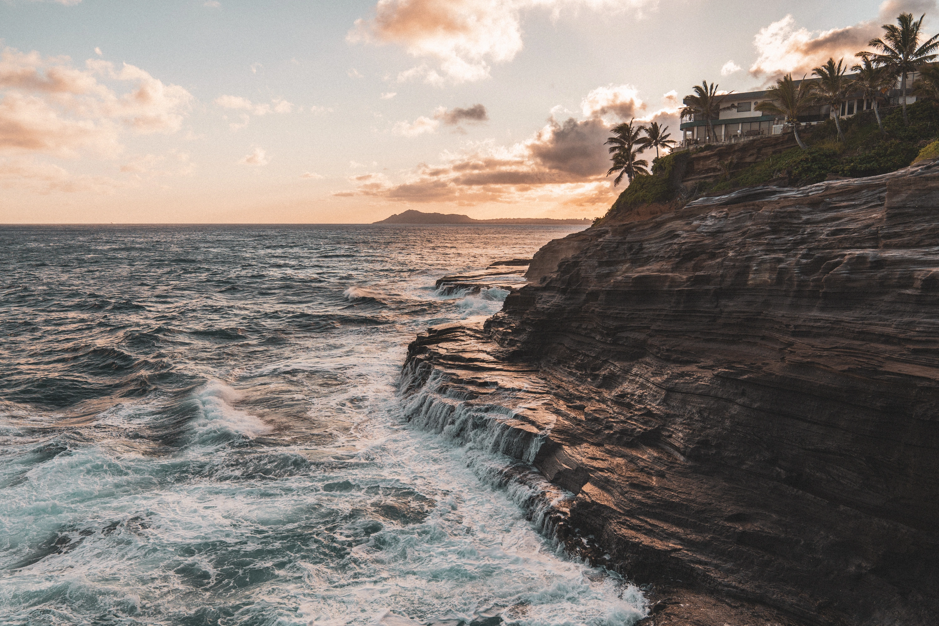 Warm sunset light above waves and layered rock at Spitting Caves
