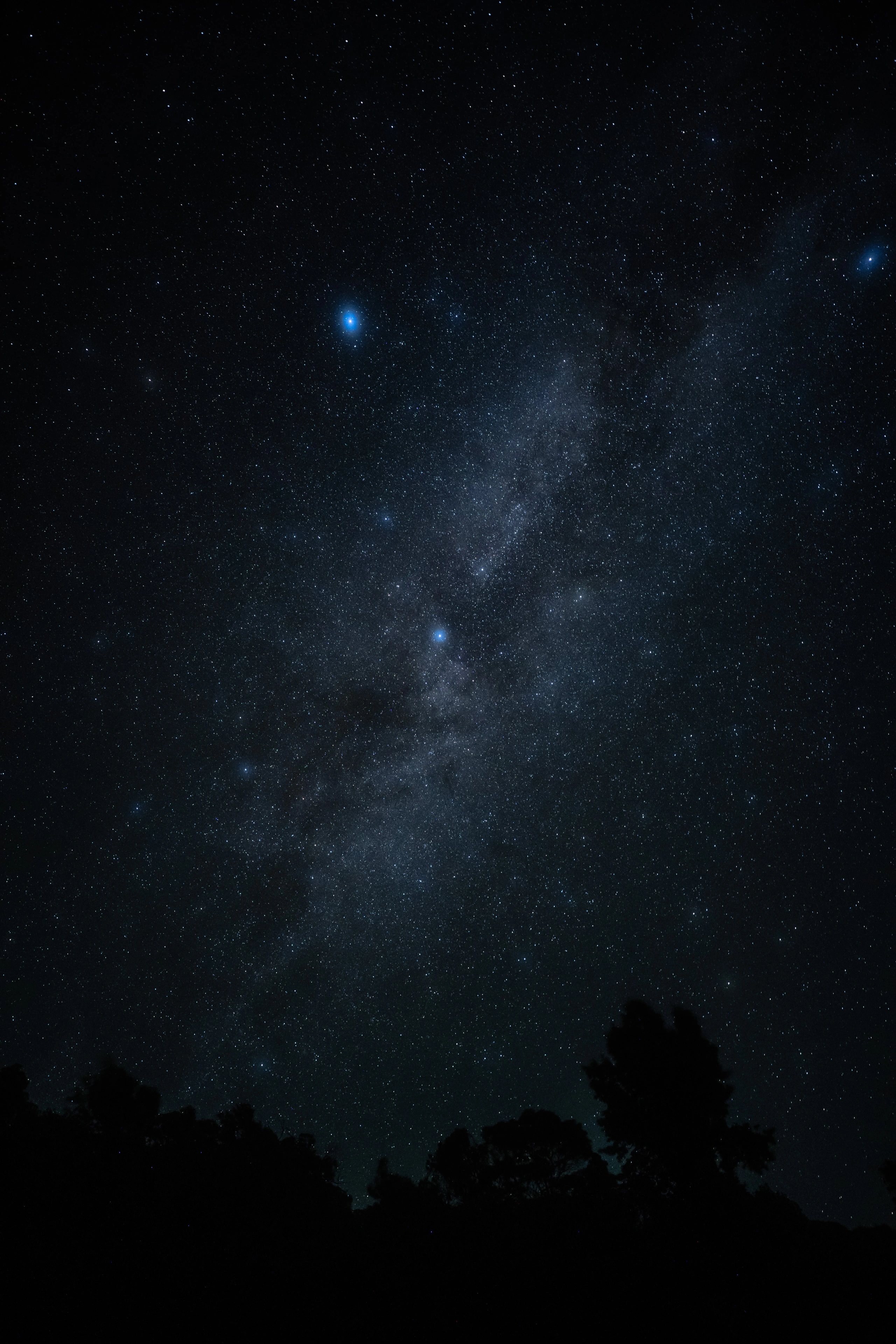 A column of Milky Way stars above a dark Waimea Canyon tree line
