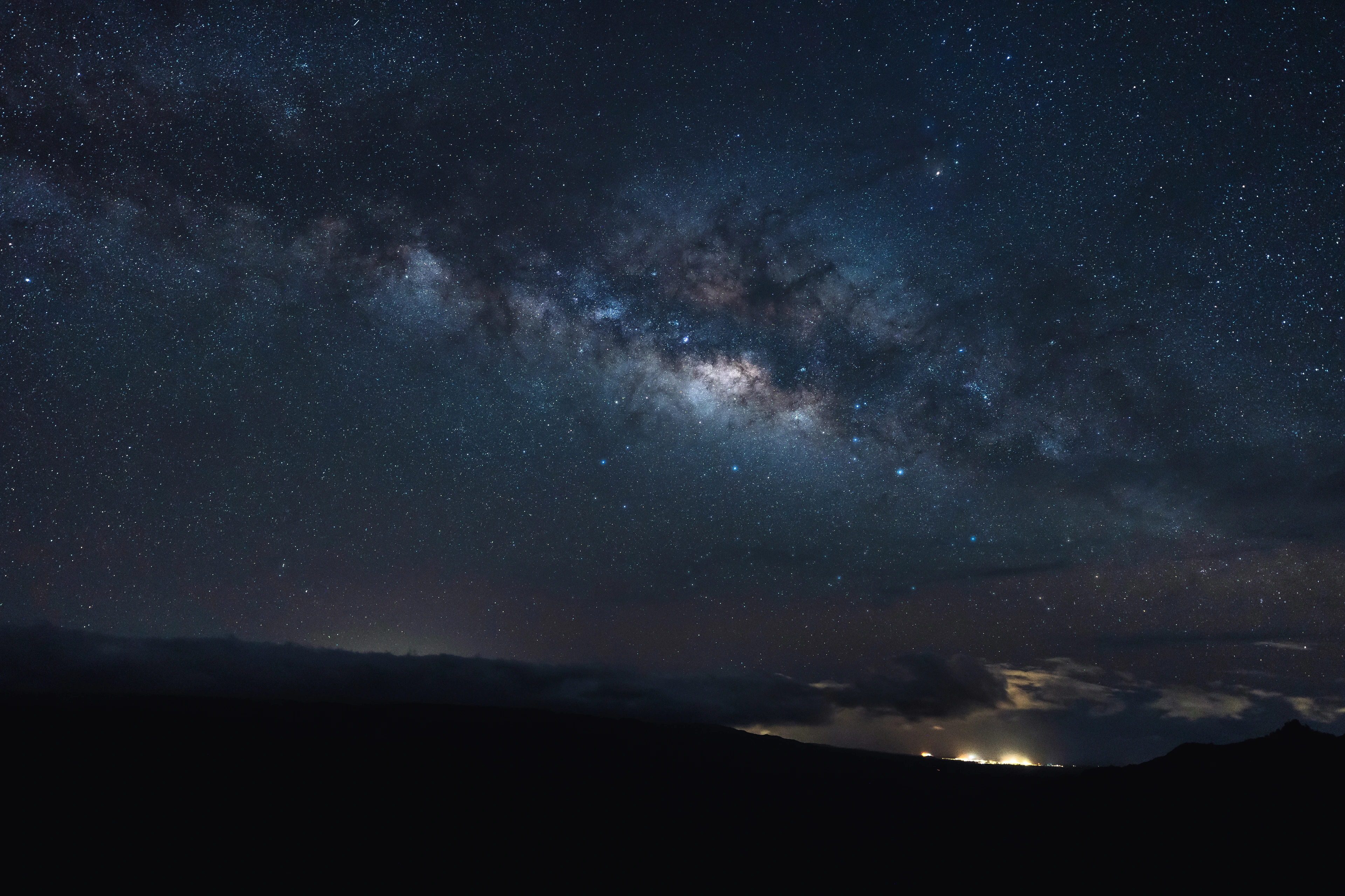 The Milky Way arching above the dark rim and distant lights of Waimea Canyon