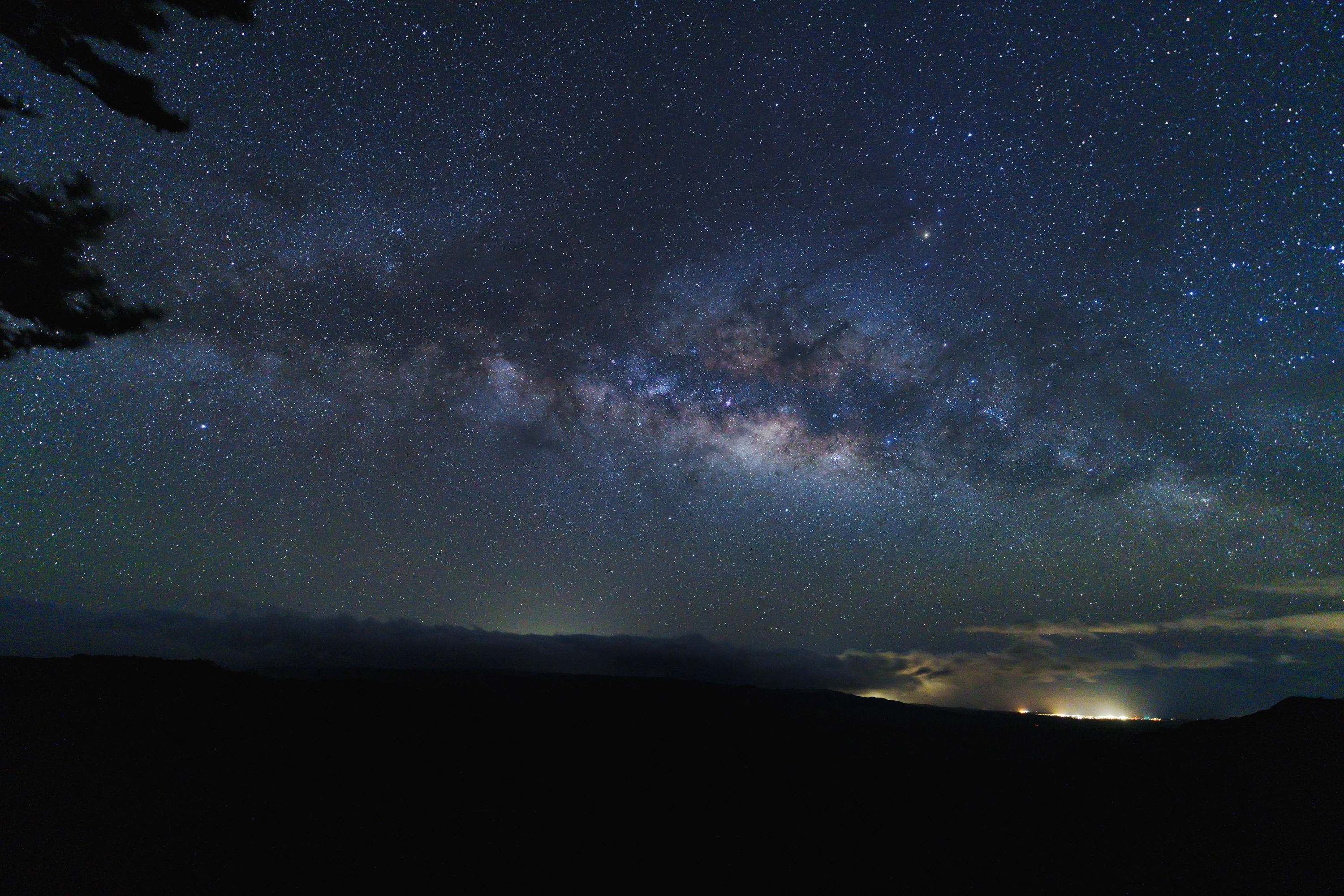 The Milky Way arching over distant lights beyond Waimea Canyon
